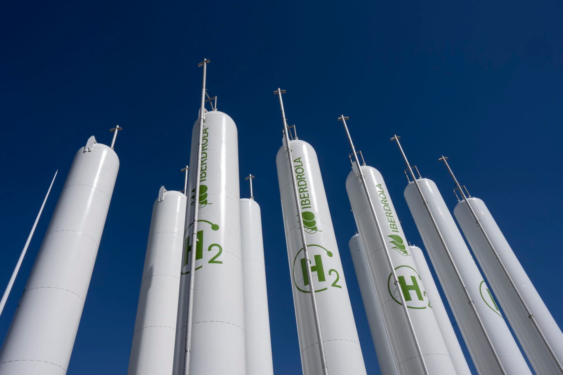 Høye, hvite, sylindriske hydrogentanker merket «H2» og «Iberdrola» står mot en klar, blå himmel.