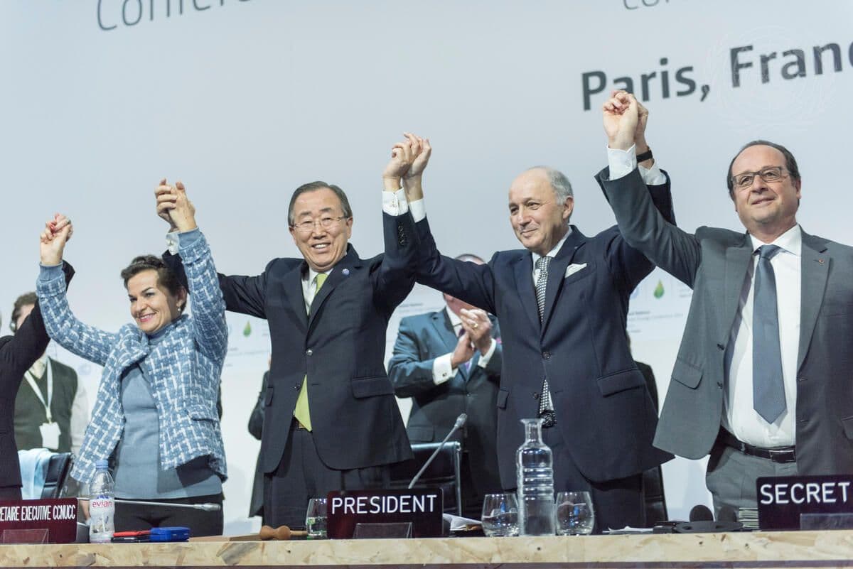 Fire tjenestemenn står bak et bord med hendene hevet til feiring på en konferanse i Paris. På skiltene på bordet står det "EXECUTIVE", "PRESIDENT" og "SECRET".
