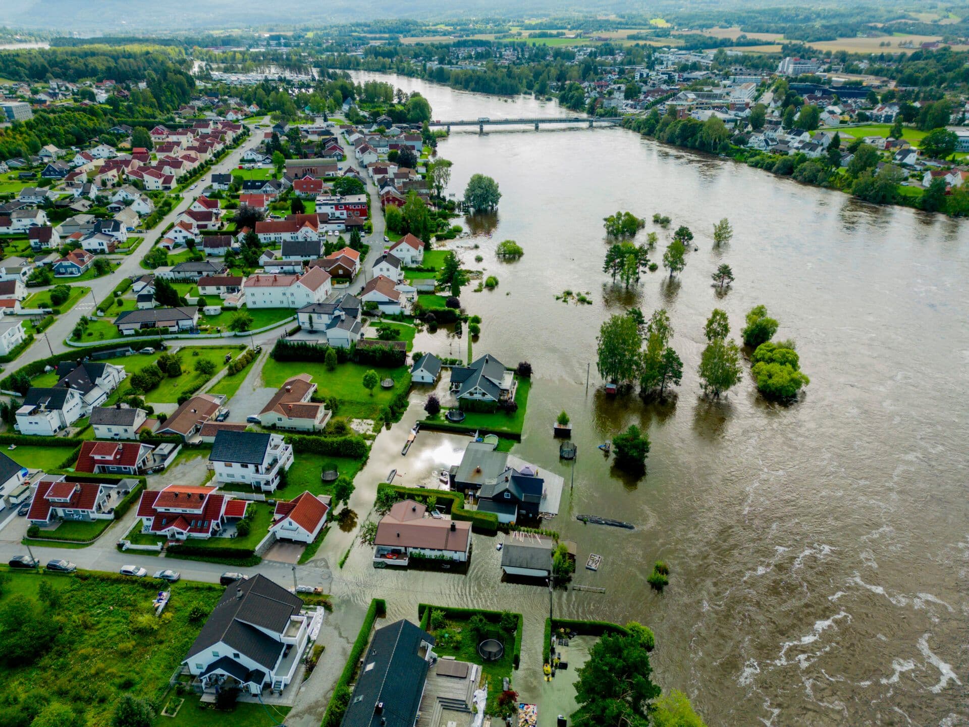 Flyfoto av et boligområde med oversvømte gater og en nærliggende elv som renner over i de omkringliggende områdene.